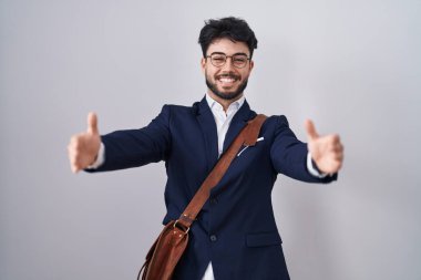 Sakallı, iş kıyafetleri giyen, kameraya bakıp sarılmak için kollarını açmış gülümseyen İspanyol bir adam. Mutluluğu kucaklayan neşeli bir ifade.. 