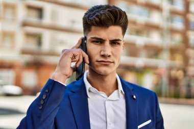 Akıllı telefondan konuşan genç adam sokakta takım elbise giyiyor.