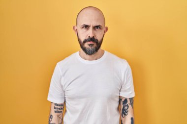 Sarı arka planda duran İspanyol dövmeli genç adam yüzünde ciddi bir ifadeyle rahatladı. Basit ve doğal bir şekilde kameraya bakıyorsun.. 