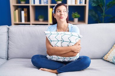 Kanepede oturup gülümseyen, yan bakan ve düşünen Latin kökenli genç kadın.. 