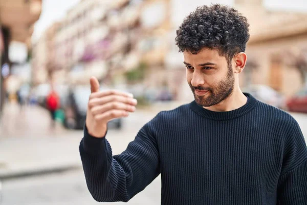 Young arab man smiling confident doing coming gesture with finger at street