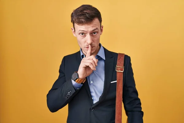 Caucasian business man over yellow background asking to be quiet with finger on lips. silence and secret concept.