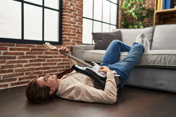 Young caucasian man playing electrical guitar lying on floor at home