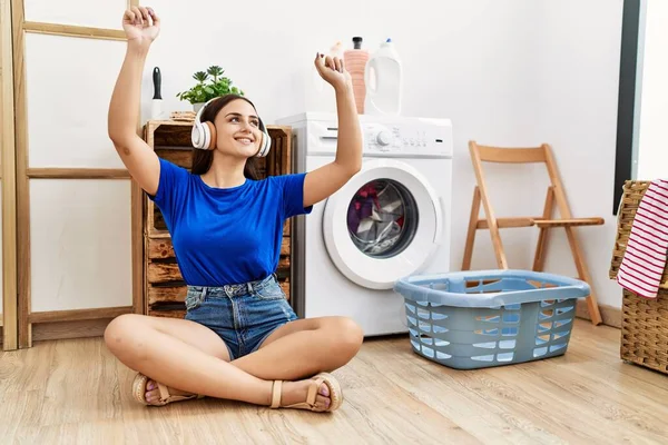 洗濯室で洗濯機を待っている音楽を聞いている若い白人女性 — ストック写真