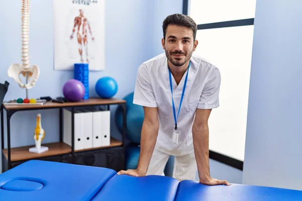 Young Hispanic Man Wearing Physiotherapist Uniform Leaning Massage Table Rehab — Stockfoto