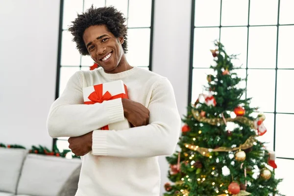 Joven Afroamericano Hombre Sosteniendo Regalo Pie Junto Árbol Navidad Casa —  Fotos de Stock