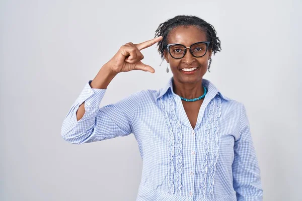 African woman with dreadlocks standing over white background wearing glasses smiling and confident gesturing with hand doing small size sign with fingers looking and the camera. measure concept.