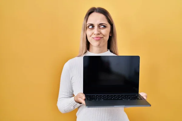 年轻的金发女人拿着笔记本电脑 面带微笑地看着旁边 望着别处 想着心事 — 图库照片