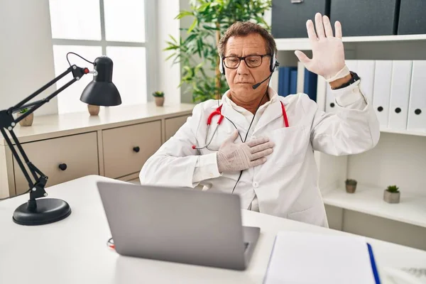 Senior doctor man working on online appointment swearing with hand on chest and open palm, making a loyalty promise oath