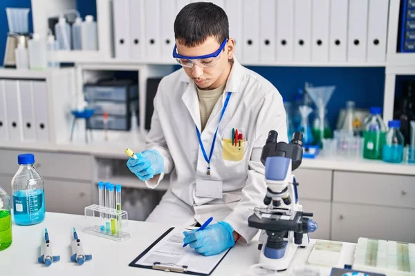 研究室で液体を測定する文書を書く若い男科学者 — ストック写真