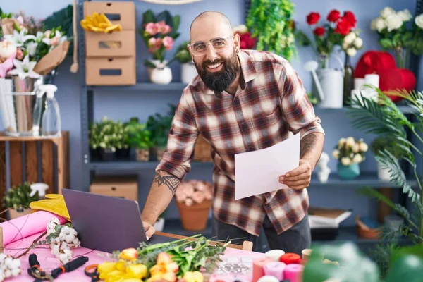 Young bald man florist using laptop reading document at flower shop