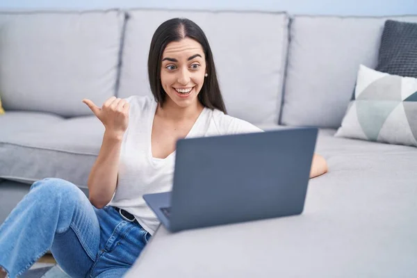 Joven Morena Usando Laptop Casa Apuntando Pulgar Hacia Lado Sonriendo — Foto de Stock