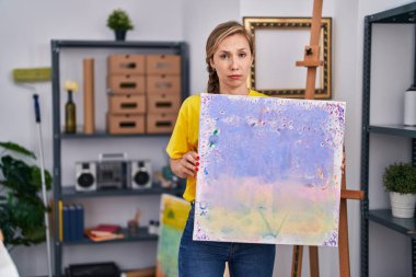 Elinde tuval tutan genç sarışın kadın şüpheci ve gergin, sorun yüzünden surat asıyor. negatif kişi. 