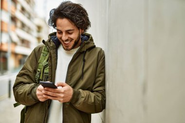 Duvara dayanmış akıllı telefon kullanan yakışıklı İspanyol.