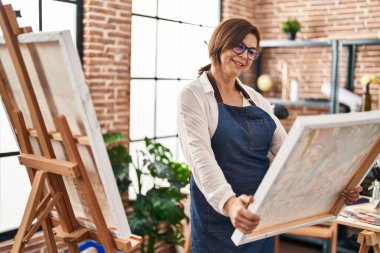 Middle age woman artist smiling confident looking draw at art studio