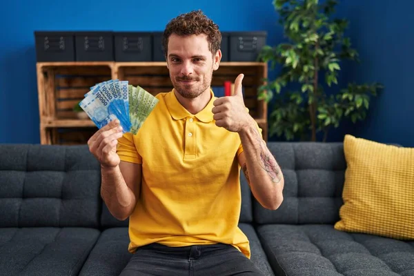 Young Hispanic Man Holding Chilean Pesos Smiling Happy Positive Thumb — Stockfoto