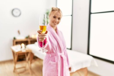 Young caucasian woman wearing bathrobe drinking champagne at beauty salon