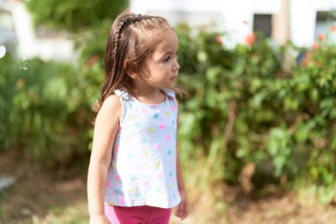 Adorable hispanic girl looking to the side with serious expression at park
