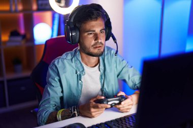 Young hispanic man streamer playing video game using joystick at gaming room