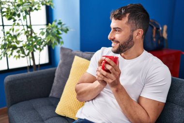 Genç İspanyol adam evdeki kanepede kahve içiyor.