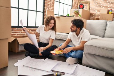 Erkek ve kadın, gülümseyen ve kendine güvenen bir çift yeni evinde boya rengi seçiyor.