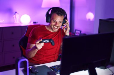 Young hispanic man streamer playing video game using joystick at gaming room