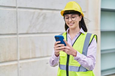 Young hispanic woman architect using smartphone at street