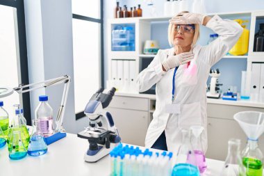 Middle age blonde woman working at scientist laboratory touching forehead for illness and fever, flu and cold, virus sick 