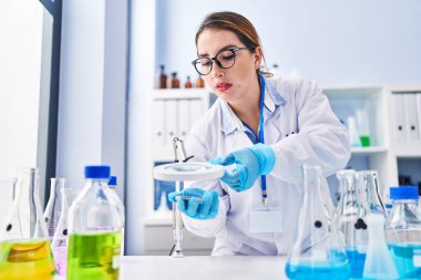 Young beautiful hispanic woman scientist using magnifying glass at laboratory