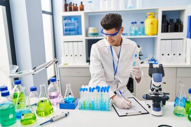 Laboratuvarda panoya yazı yazan, bilim adamı üniforması giyen İspanyol bir genç.