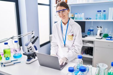 Young caucasian woman scientist smiling confident using laptop at laboratory