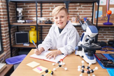 Sevimli çocuk, gülümseyen, kendine güvenen sınıftaki not defterine yazan öğrenci.