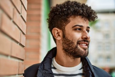 Duvara yaslanmış gülümseyen genç bir Arap.