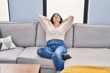 Young chinese woman relaxed with hands on head sitting on sofa at home