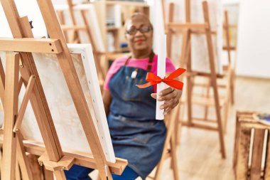 Senior african american woman smiling confident holding diploma at art studio