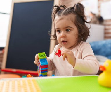 Adorable hispanic girl playing with construction blocks standing at kindergarten
