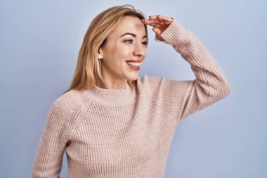 Mavi arka planda dikilen İspanyol kadın çok mutlu ve gülümsüyor. arama kavramı. 