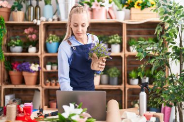 Young blonde woman florist using laptop holding lavender plant at florist