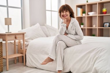 Orta yaşlı kadın yatakta kendinden emin bir şekilde gülümsüyor.