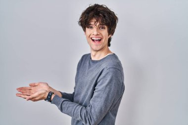 İzole edilmiş arka planda duran genç adam avuçlarını açıp fotokopi alanını gösteriyor, gülümseyerek mutlu bir şekilde gülümsüyor. 