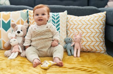 Sevimli kızıl saçlı bebek gülümsüyor. Evdeki kanepede otururken kendine güveniyor.