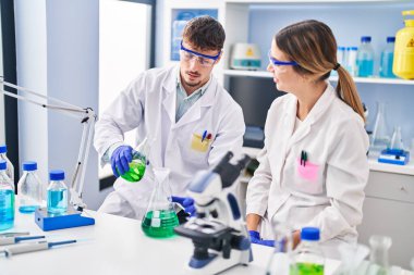 Young man and woman scientists workers measuring liquid at laboratory