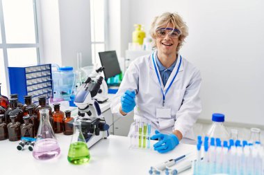 Laboratuvarda test tüpüne sıvı döken genç sarışın bilim adamı.