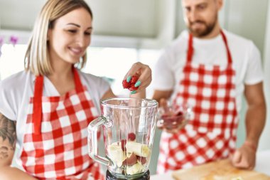 Genç çift gülümsüyor. Mutfakta smoothie pişiriyorlar.