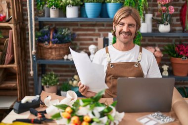 Çiçekçide dizüstü bilgisayar okuyan genç sarışın bir çiçekçi.