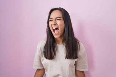 Genç İspanyol kadın pembe arka planda kızgın ve kızgın bağırıyor sinirli ve öfkeli, öfkeyle bağırıyor. öfke ve agresif konsept. 