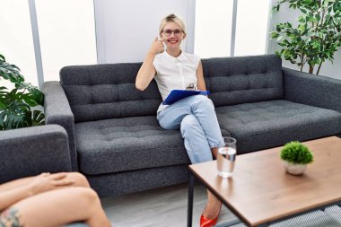 Young psychologist woman at consultation office pointing with hand finger to face and nose, smiling cheerful. beauty concept 