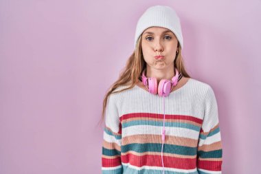 Young blonde woman standing over pink background puffing cheeks with funny face. mouth inflated with air, crazy expression. 