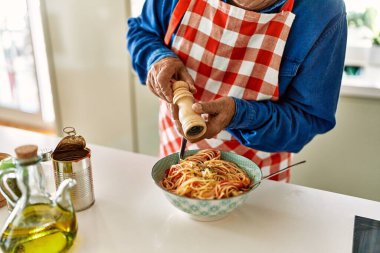 Senior man pouring pepper on spaghetti at kitchen