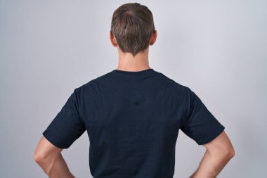 Caucasian blond man wearing bitcoin t shirt standing backwards looking away with arms on body 